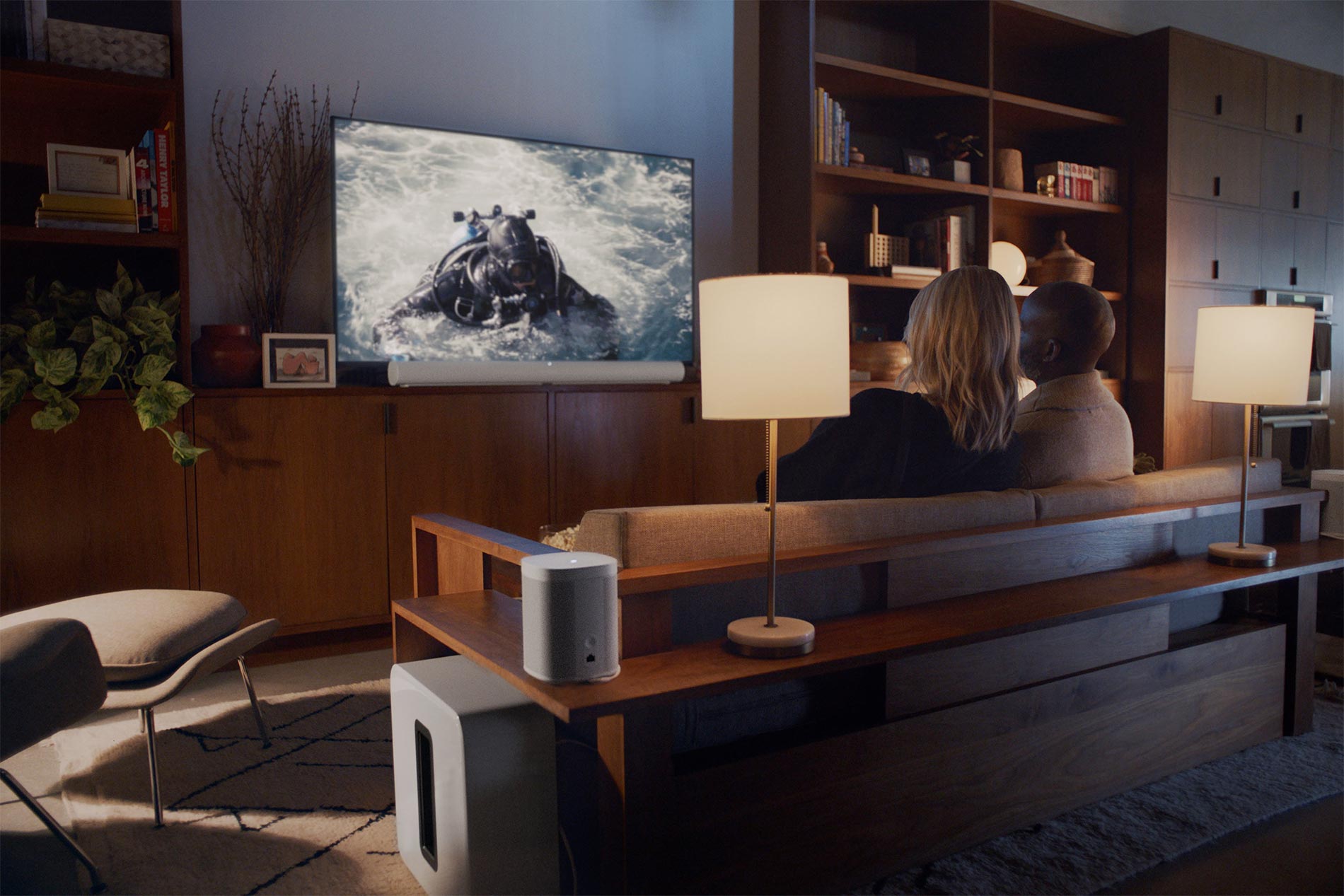 Couple sitting on sofa watching movie on large TV in cozy living room